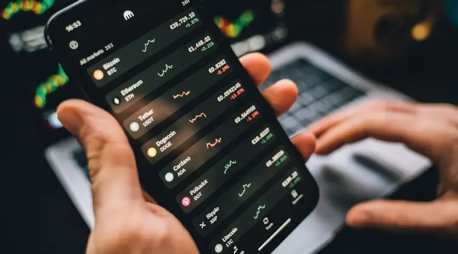 Person holding smartphone showing cryptocurrency market data, symbolizing digital investment tools.