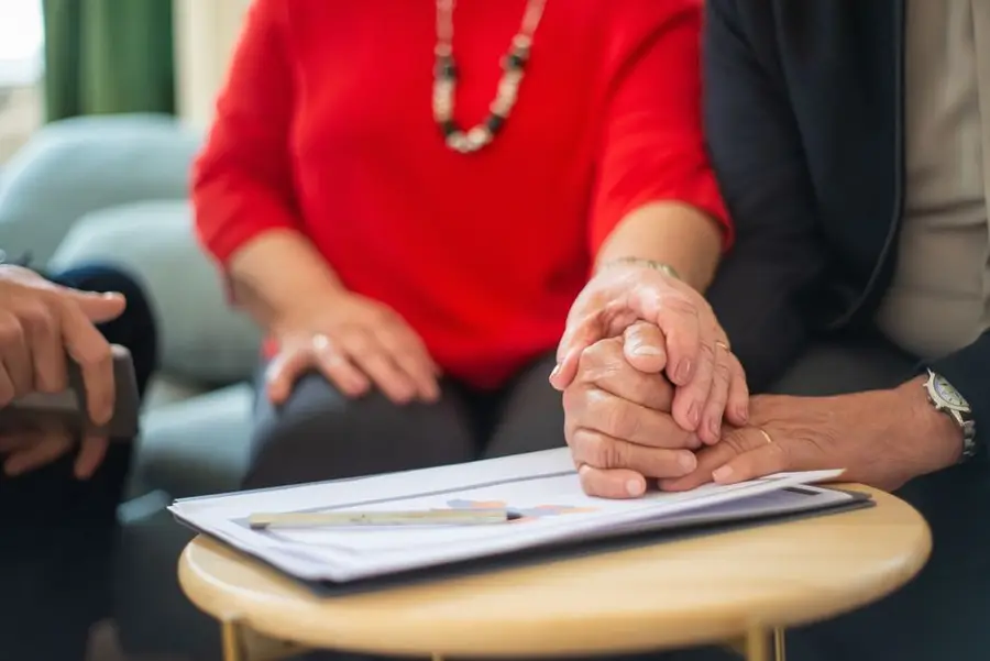 Senior couple holding hands over a table with documents, symbolizing support in an office setting.