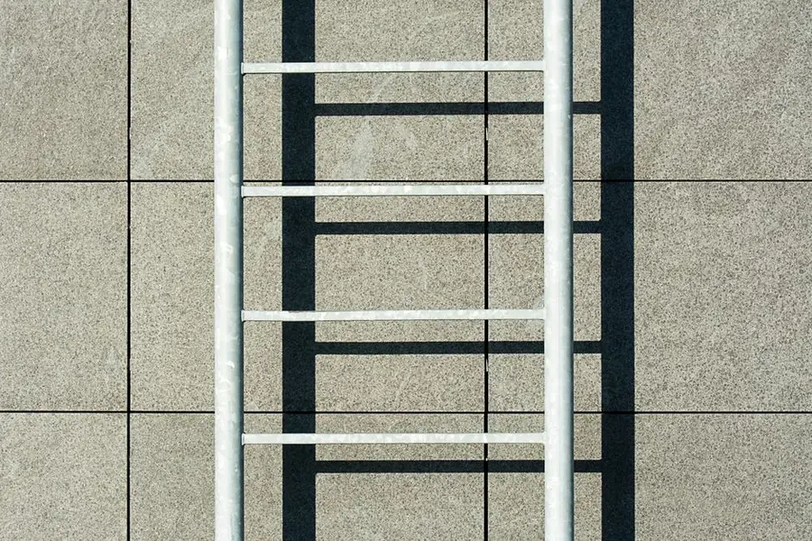 A striking minimalist photo of a ladder casting a shadow on a tiled wall.