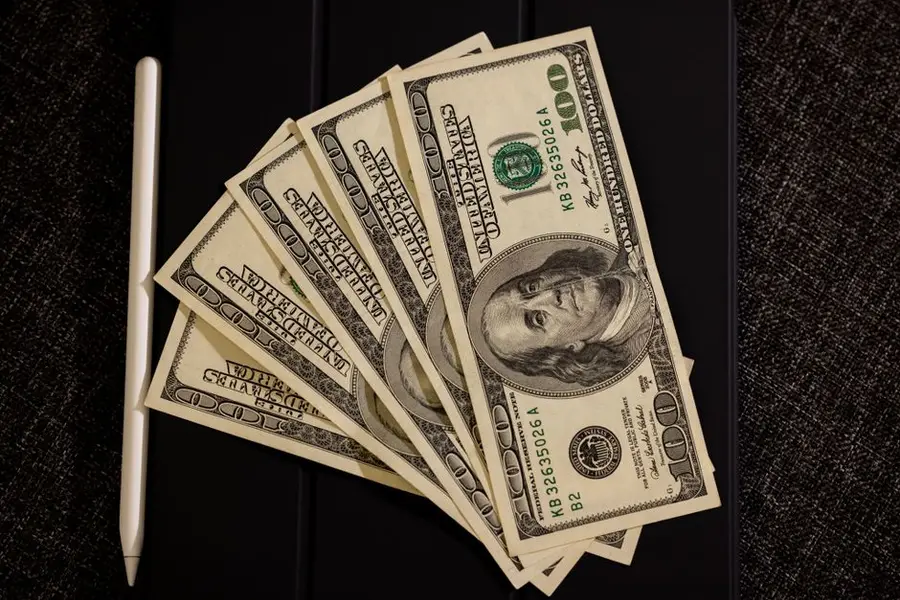 Spread of US dollar bills on black surface with stylus, symbolizing finance and technology.