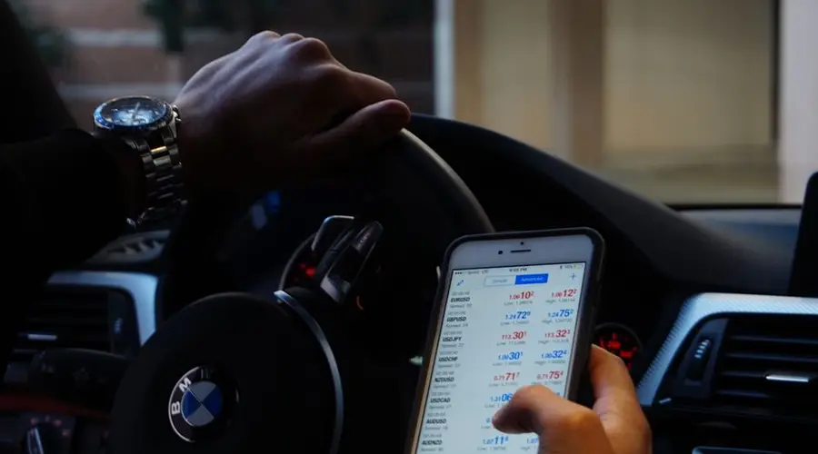 Person using mobile phone for currency trading while driving BMW car.