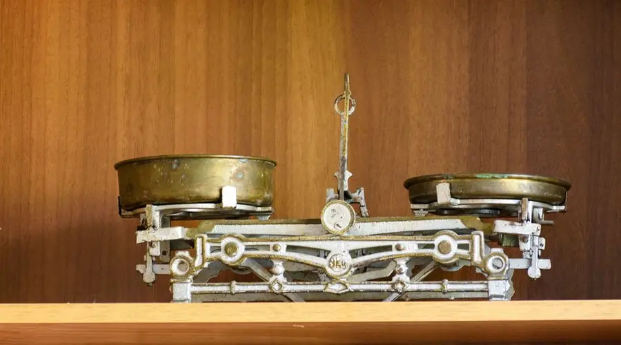 Retro brass kitchen balance scale with symmetry displayed on wooden shelf.