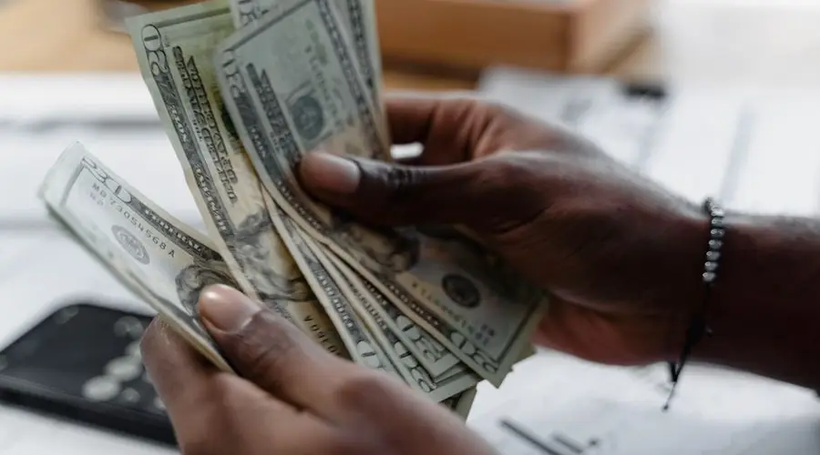 Detailed image of hands counting US dollar bills on a desk, emphasizing finance and budgeting.