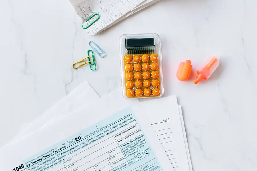 A flat lay image of tax forms, calculator, and office supplies on a desk.