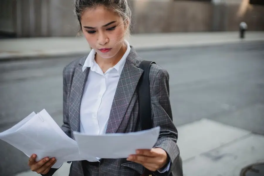 Focused businesswoman in a suit reviews important papers outdoors.