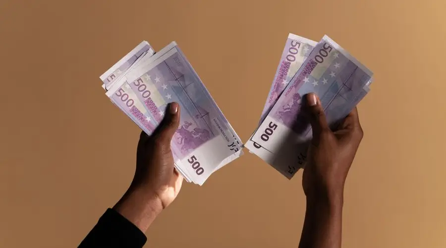 Close-up image of hands holding 500 euro banknotes on a neutral beige background.