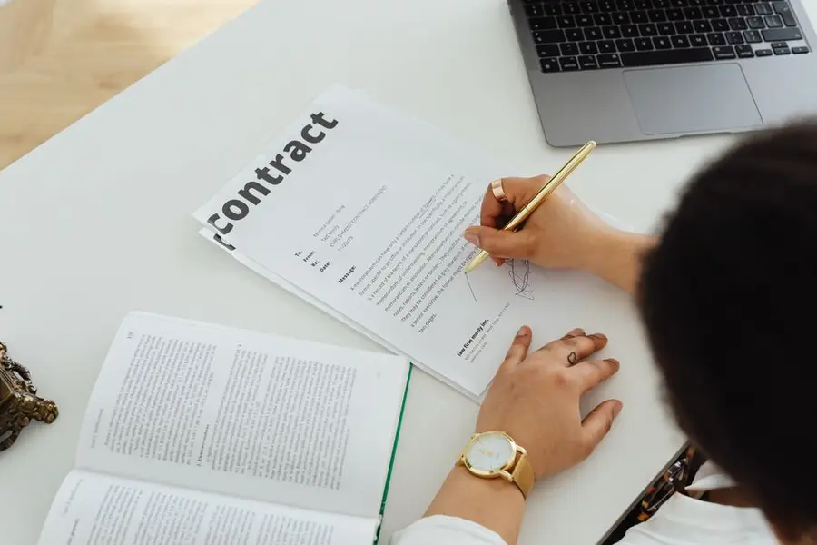 Professional signing a business contract at a modern desk setup for office work.