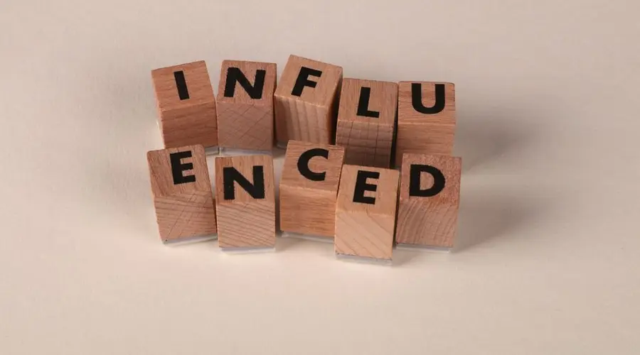 Wooden letter blocks arranged to spell 'Influenced' on a neutral beige surface.
