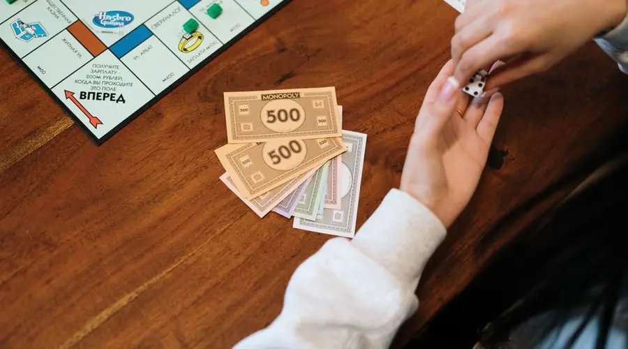 Hands holding dice near Monopoly board with fake money on table.