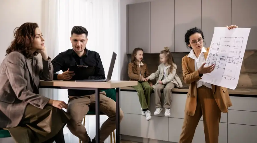 Real estate agent presenting house plans to clients in a modern kitchen setting.