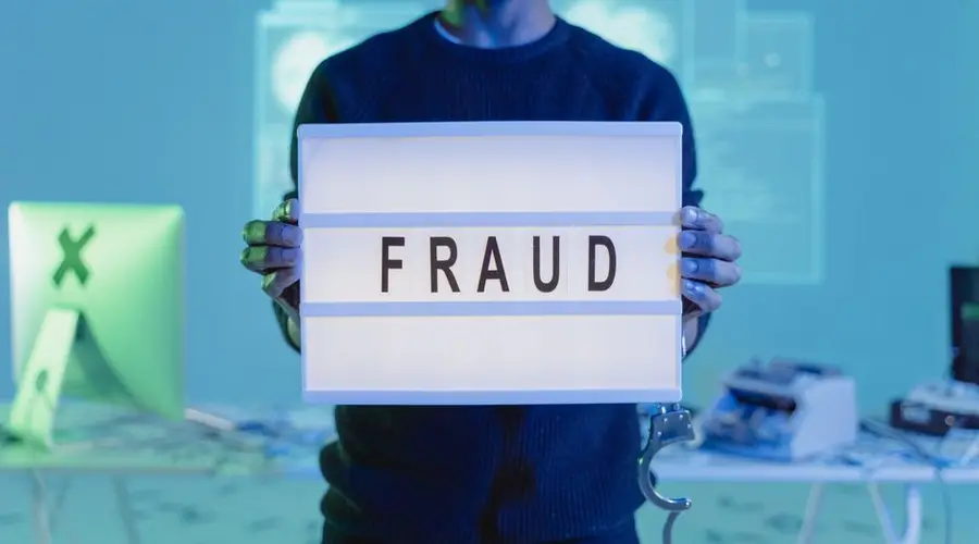 A man holding a sign reading 'FRAUD' in a tech environment, highlighting cybersecurity concerns.