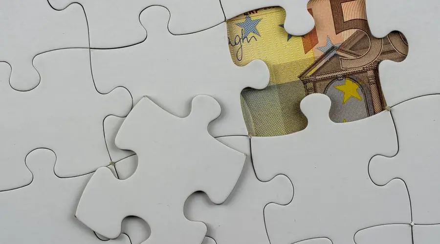 Close-up of a jigsaw puzzle missing piece revealing Euro currency underneath.
