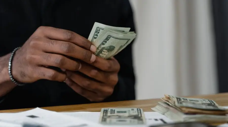 Adult counting dollar bills at a desk, focused on money management and finance.