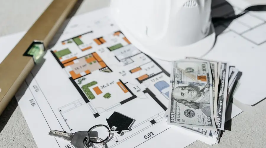 Floor plan with cash, keys, and hard hat symbolizing real estate investment and property planning.