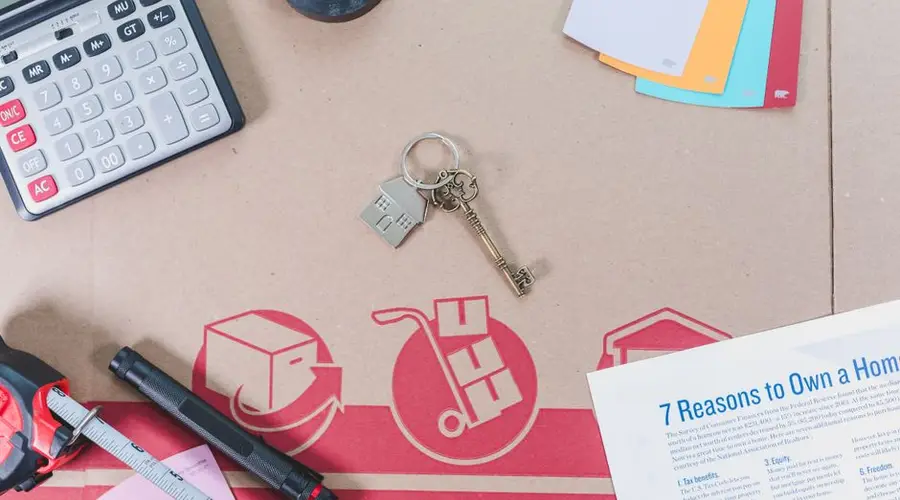 Flat lay of home buying essentials with calculator, keys, tape, and color swatches.