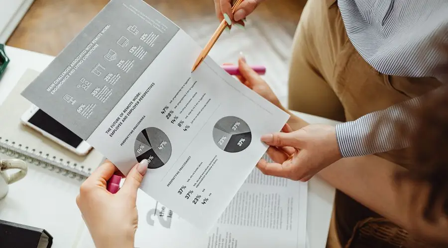Two people reviewing financial reports and graphs at a desk for analysis and decision-making.
