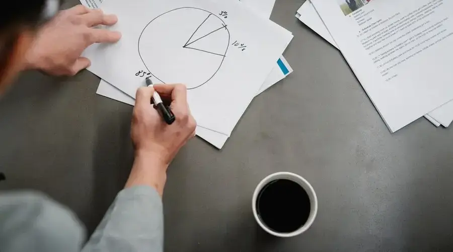 Man drawing a pie chart on paper with coffee, representing business planning and analysis.