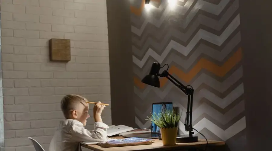 A young boy focuses on online classes at a desk in a cozy home setting.
