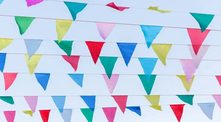 Vibrant and colorful triangular streamers hanging against a clear blue sky, celebrating festival vibes.