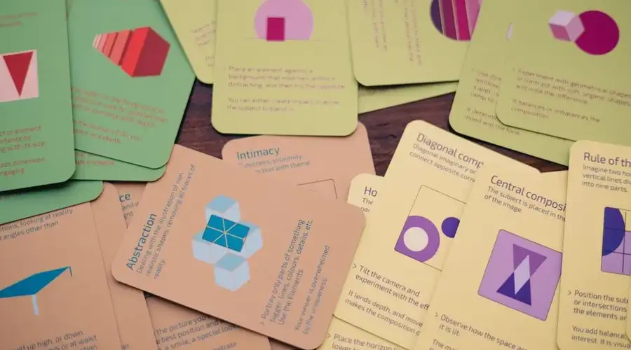 A variety of colorful game cards with geometric shapes scattered across a wooden table.