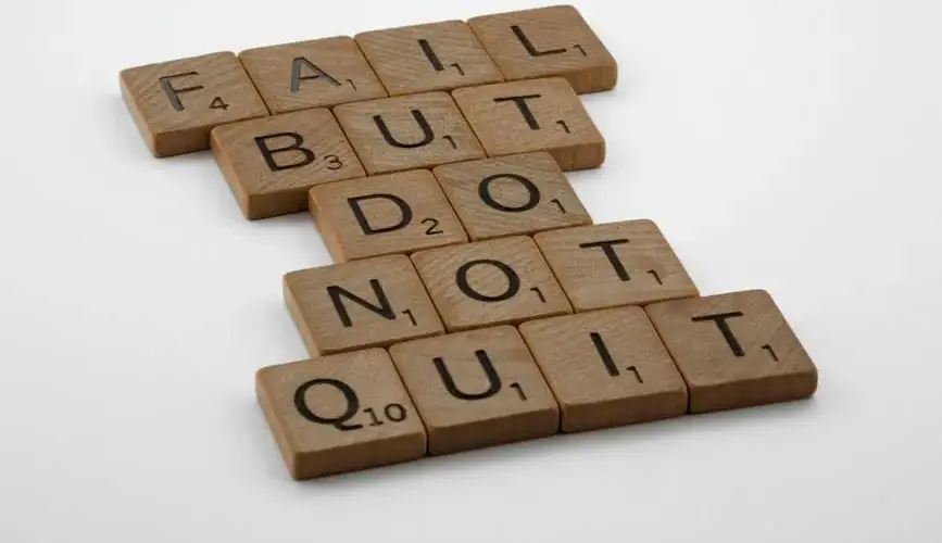 Close-up of Scrabble tiles forming the motivational phrase 'Fail but do not quit' on a white surface.