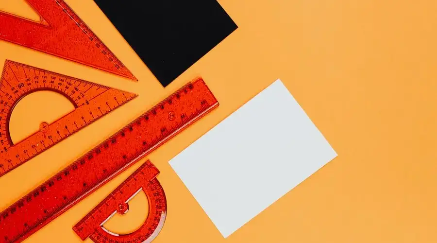 Vibrant orange rulers and geometric tools on an orange background with black and white cards.