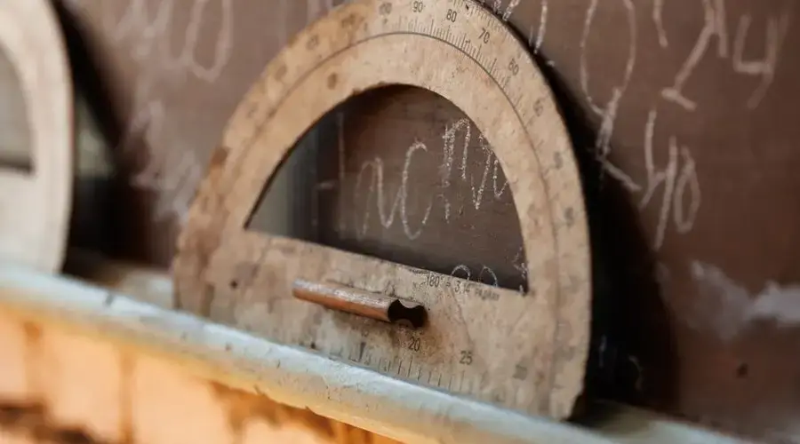 A vintage protractor resting against a chalkboard filled with chalk writing.