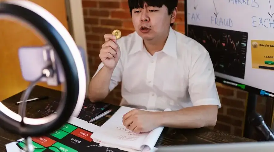 A man using a ring light and recording video about cryptocurrency markets and investments.