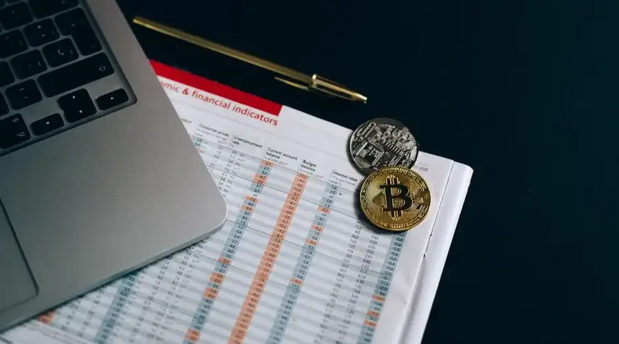 Bitcoin and cryptocurrency coins placed on a financial document next to a laptop.
