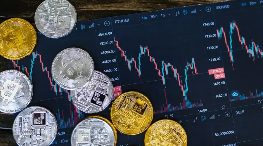 Close-up of gold and silver cryptocurrency coins on a digital trading chart.