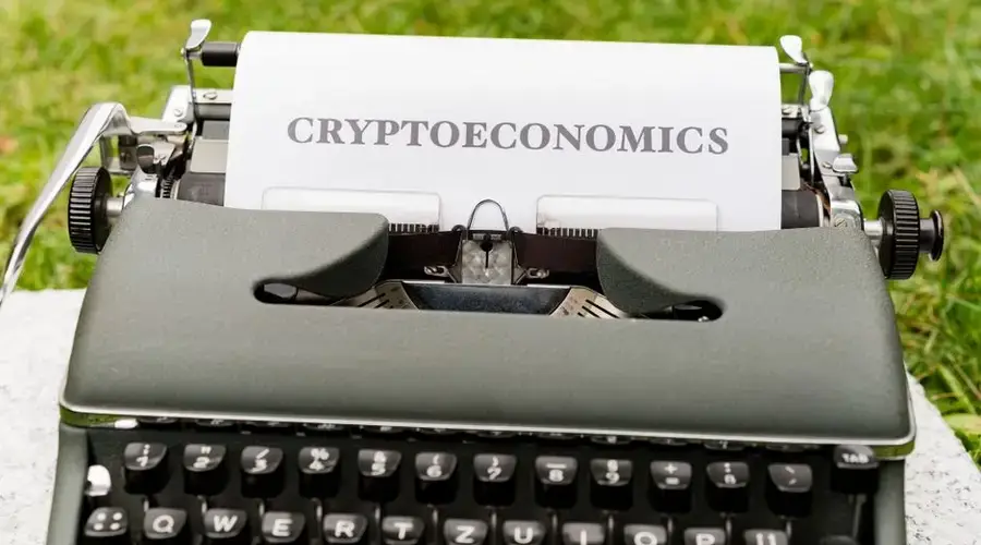 An antique typewriter with cryptoeconomics text on paper against a grassy background.