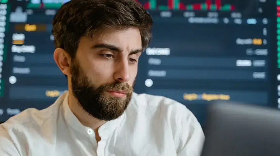 Close-up of thoughtful businessman with beard analyzing stock market data on screen.