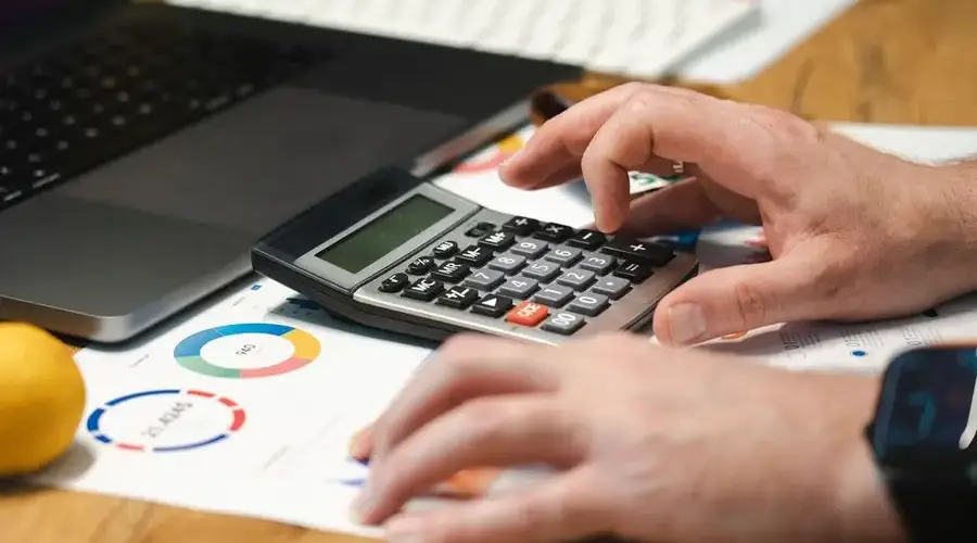 A person analyzing financial data using a calculator and laptop on a desk.