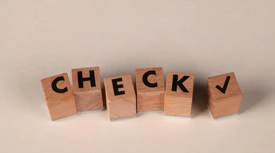 Wooden blocks aligned to spell 'CHECK' with a checkmark symbol on a neutral background.