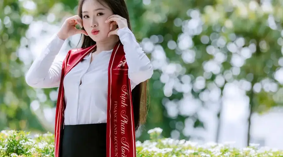 Young woman in graduation attire posing outdoors with greenery background.