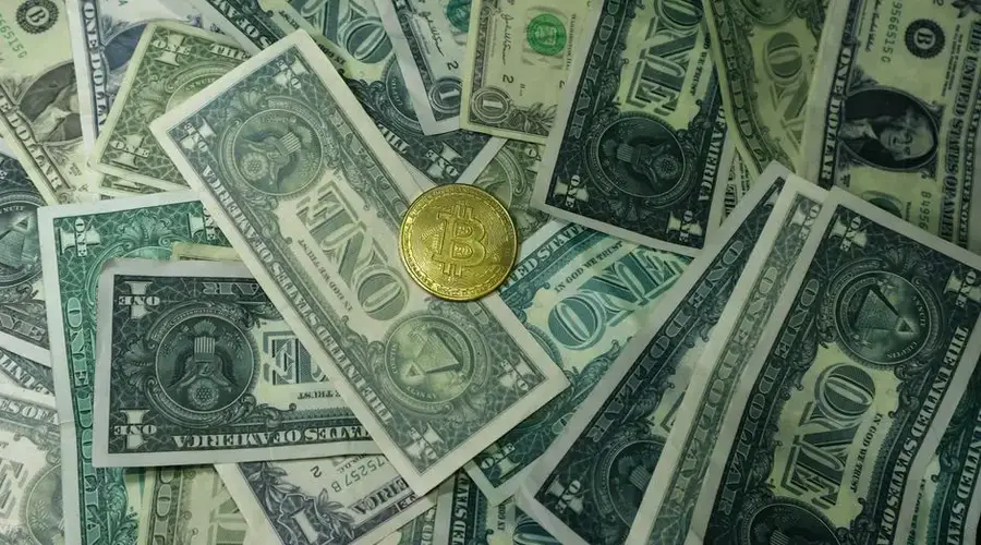 A golden bitcoin coin surrounded by scattered US dollar bills, symbolizing the contrast between digital and traditional currency.