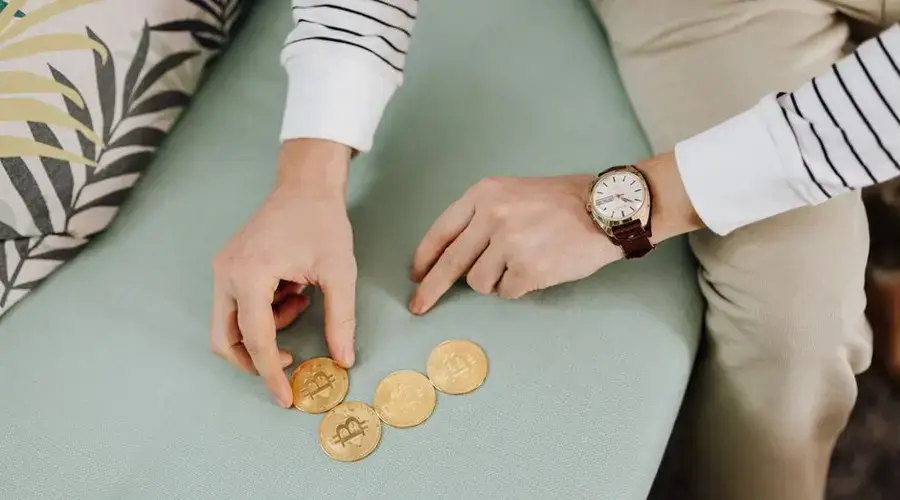 Close-up of hands holding bitcoin coins on a green sofa, emphasizing digital currency trends.