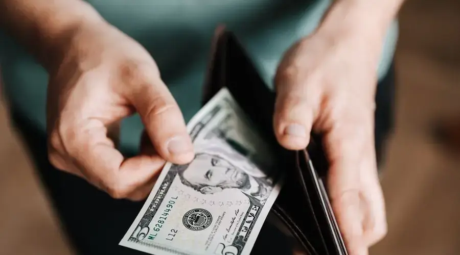 Closeup of crop male in casual clothes taking dollars out of wallet while paying in shop