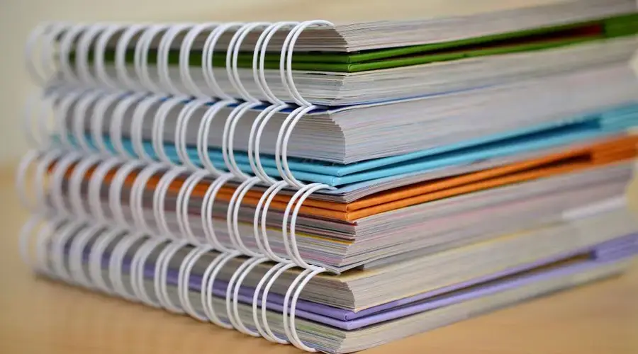 A colorful stack of spiral-bound notebooks neatly placed on a wooden desk. Ideal for educational themes.