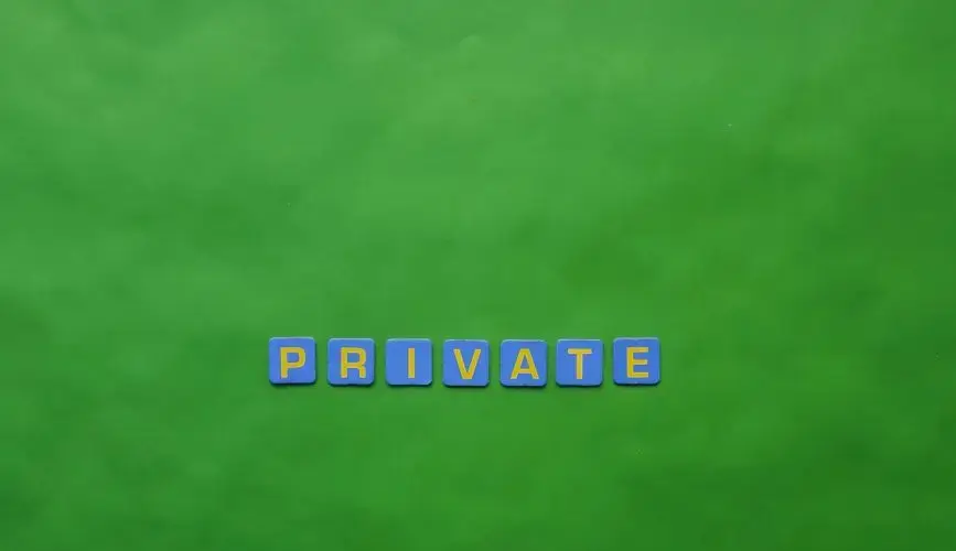 Close-up of 'PRIVATE' spelled with Scrabble tiles on a green background, emphasizing privacy.