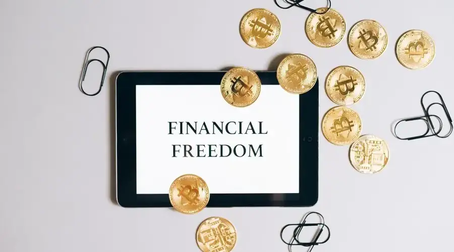 Top view of a tablet displaying 'Financial Freedom' with scattered bitcoin coins, symbolizing digital currency.