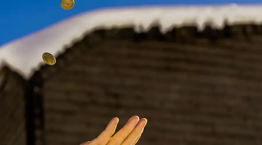Close-up of a hand flipping coins against a snowy roof and clear blue sky.