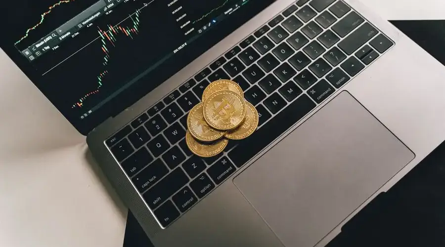 Bitcoin coins placed on a laptop keyboard while a trading chart displays on the screen, showcasing digital finance.