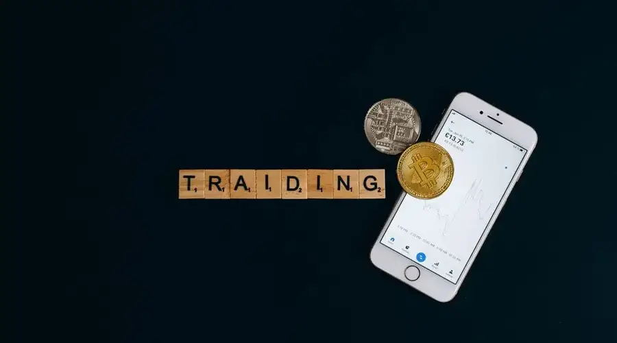 A smartphone and Bitcoin coins with trading letters on black background.