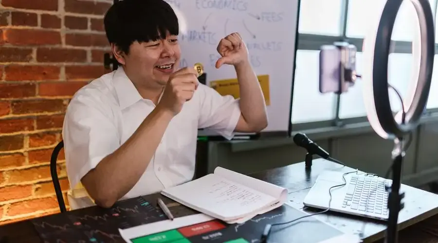 Asian male vlogger discussing cryptocurrency trading in an online video setup.