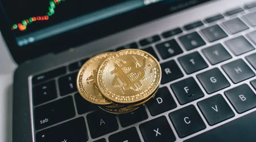 Close-up of golden bitcoins on a laptop keyboard depicting cryptocurrency and trade concepts with a market chart in the background.