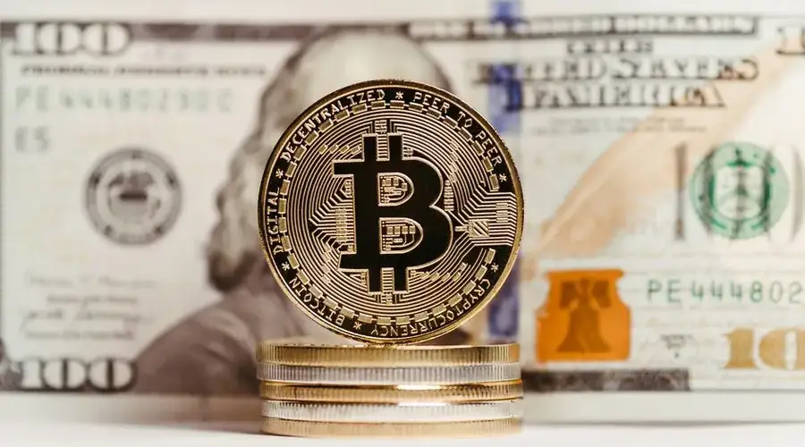 Bitcoin coin stacked with US $100 bill background, representing finance and cryptocurrency convergence.