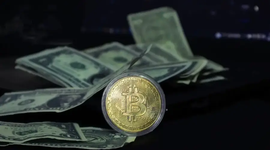 Bitcoin coin surrounded by scattered US dollar bills on a dark surface, symbolizing modern finance.
