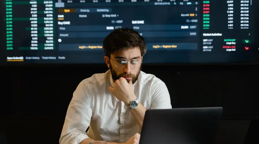 A man intensely analyzing stock market data on a laptop in an office setting.