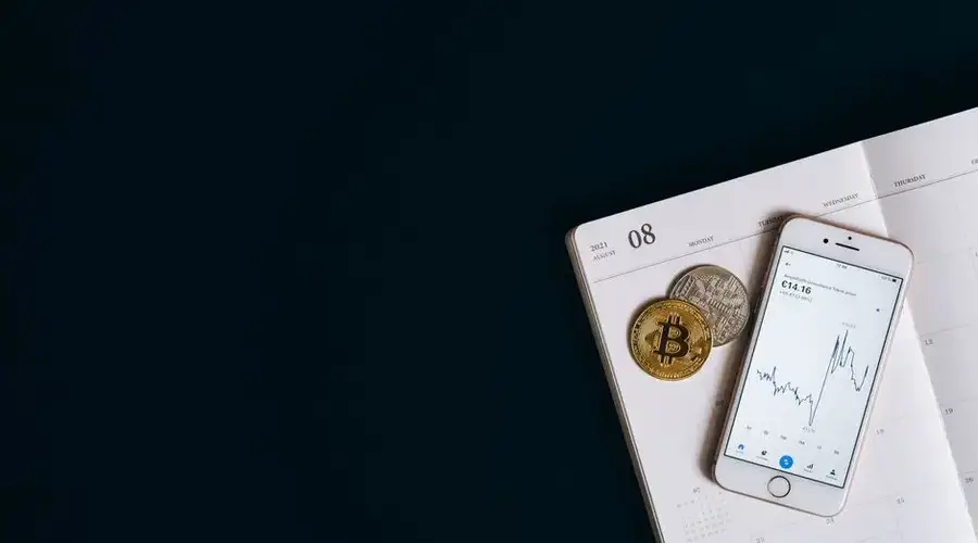 Smartphone displaying cryptocurrency data next to Bitcoin on a calendar offers finance and technology insights.